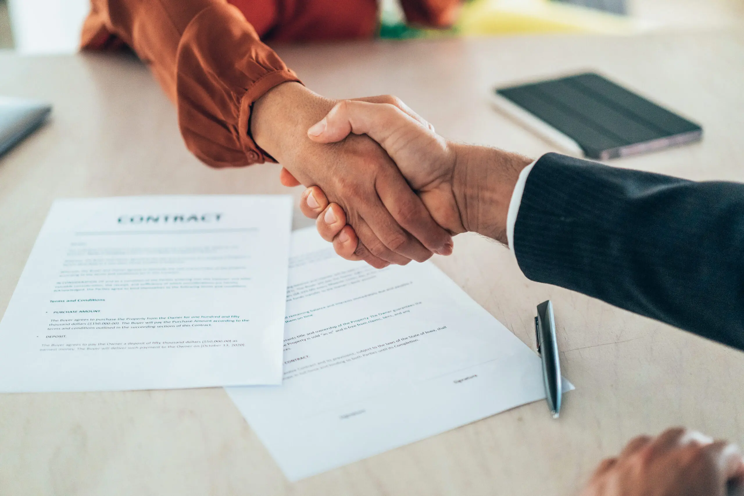 Two professionals shake hands over a signed contract, representing the successful conclusion of a business deal. This image embodies the spirit of collaboration and trust in a corporate environment.